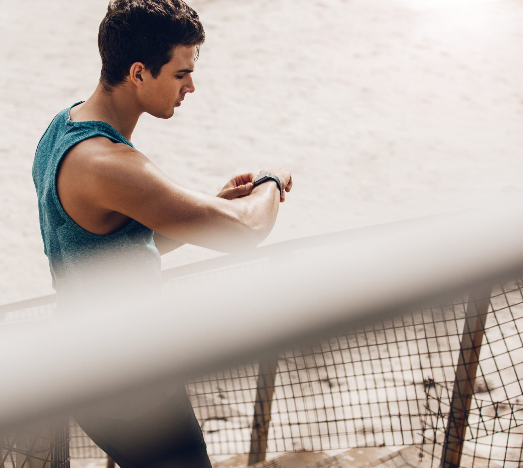 Young man standing outdoors using a smartwatch to monitor his progress. Caucasian male runner resting and checking his performance on fitness smart watch device.