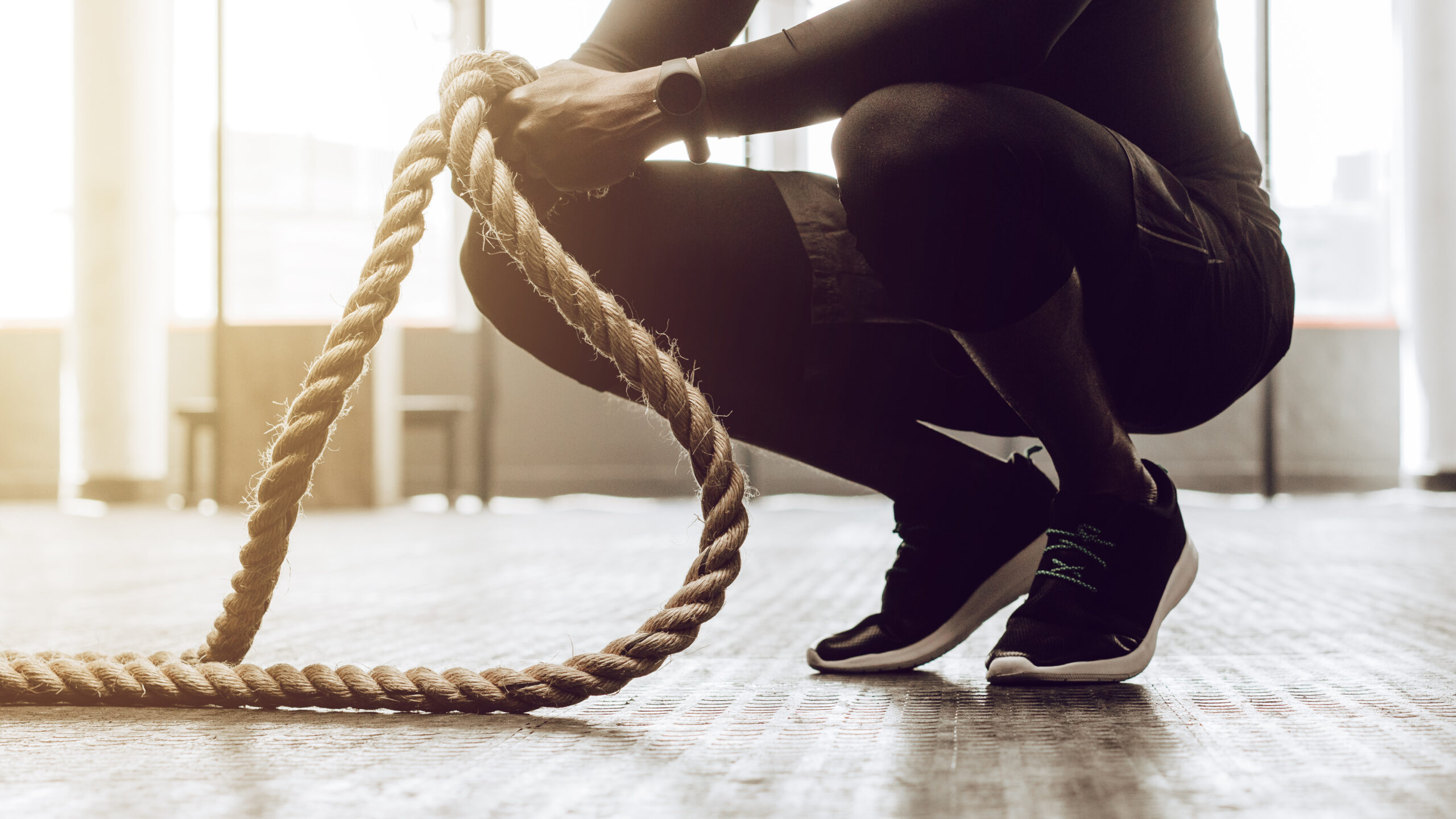 Close up of a man sitting on his toes holding a pair of battle ropes for workout. Crossfit guy at the gym working out with fitness rope.