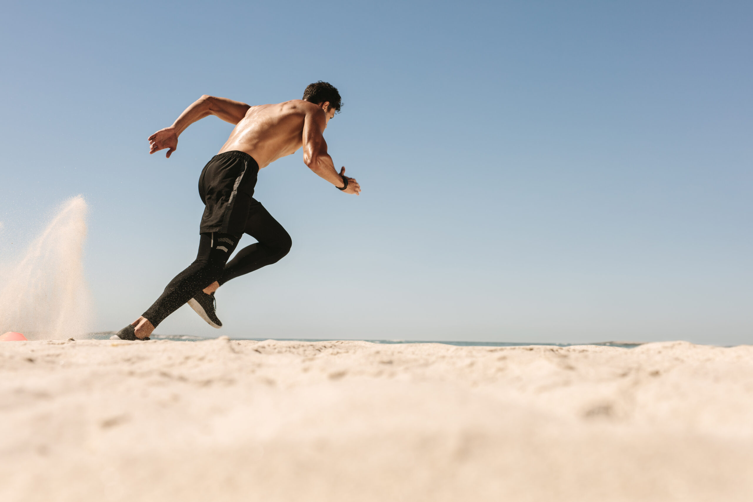 Man doing fitness workout at a beach on a sunny day. Side view of an athletic man running on the beach.