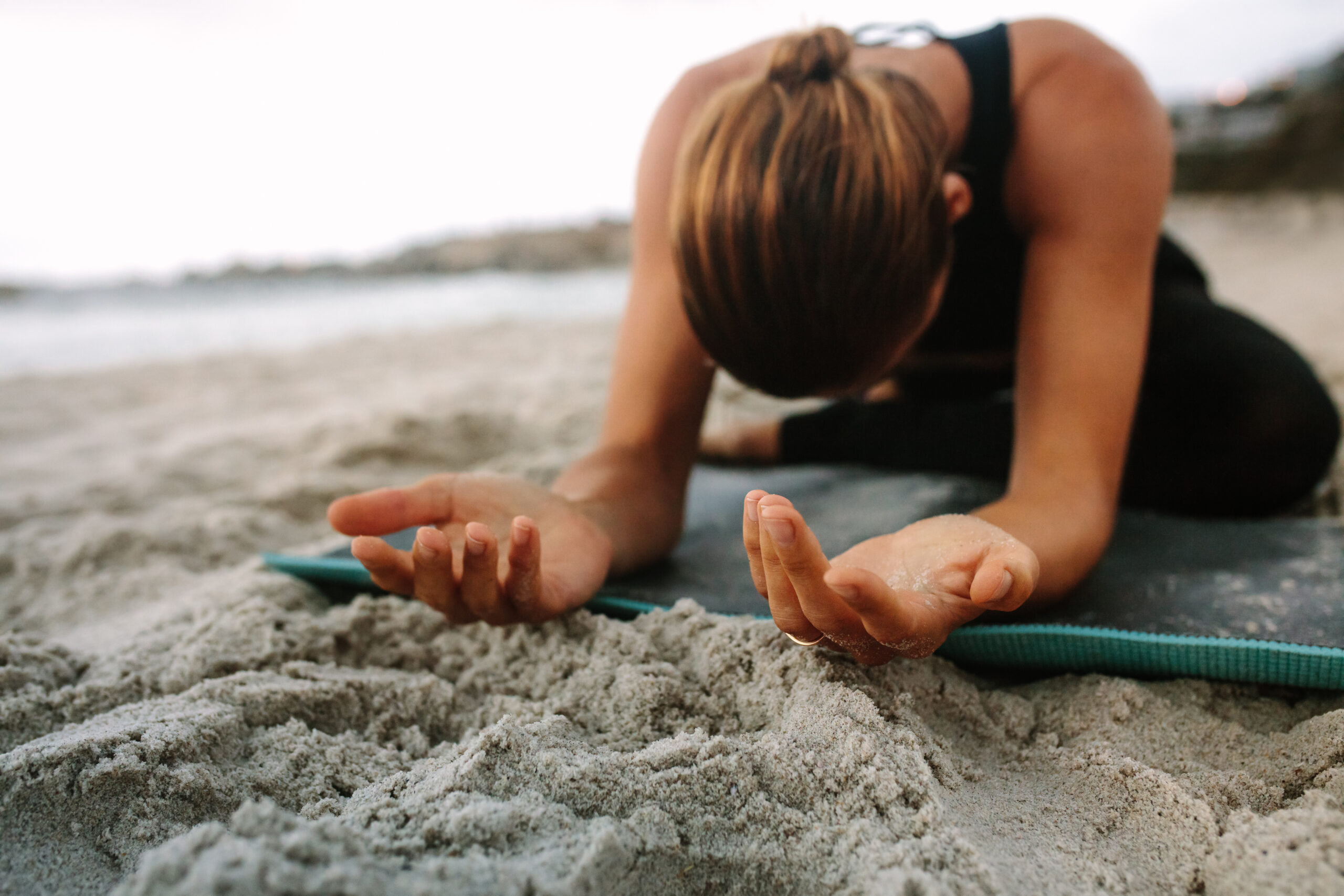 Close up of a woman sitting on a mat at the beach practicing yoga. Woman sitting at the beach in a yoga position with palms facing up.
