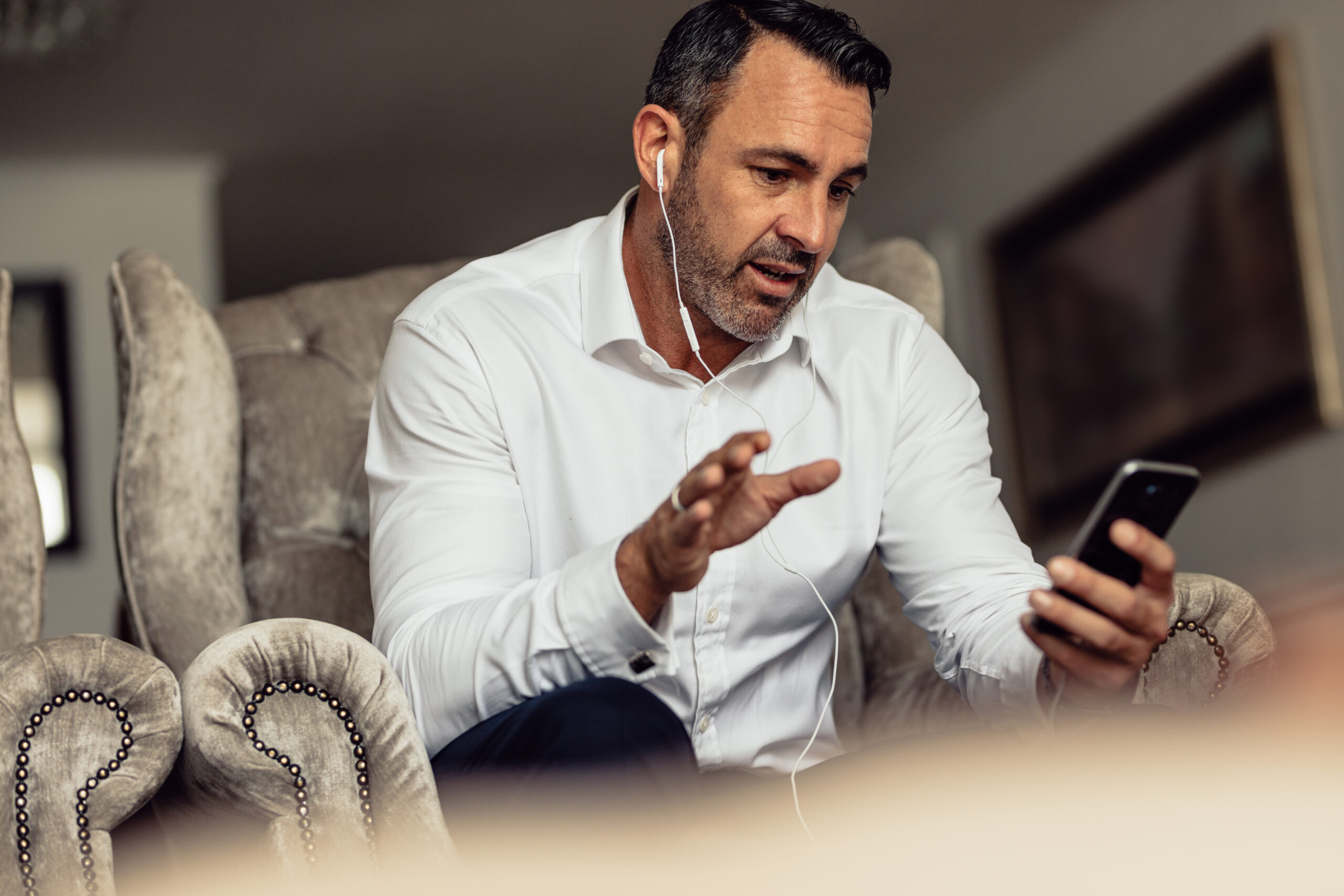 Mature businessman wearing earphones talking on mobile phone. Man on business trip sitting in hotel room and making phone call.