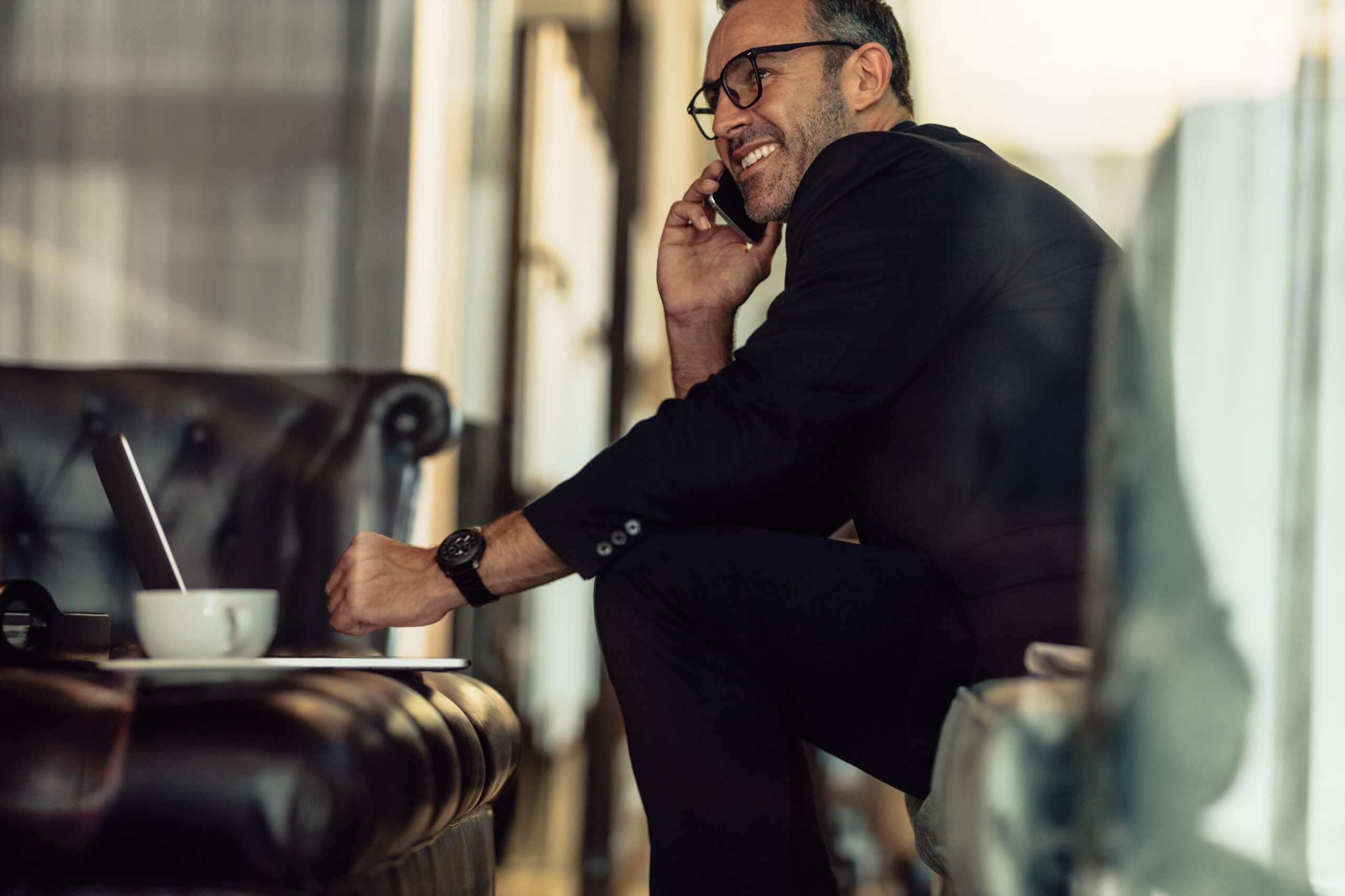 Successful mature businessman sitting in hotel lobby talking on cellphone. Happy man in business suit working from hotel lobby.