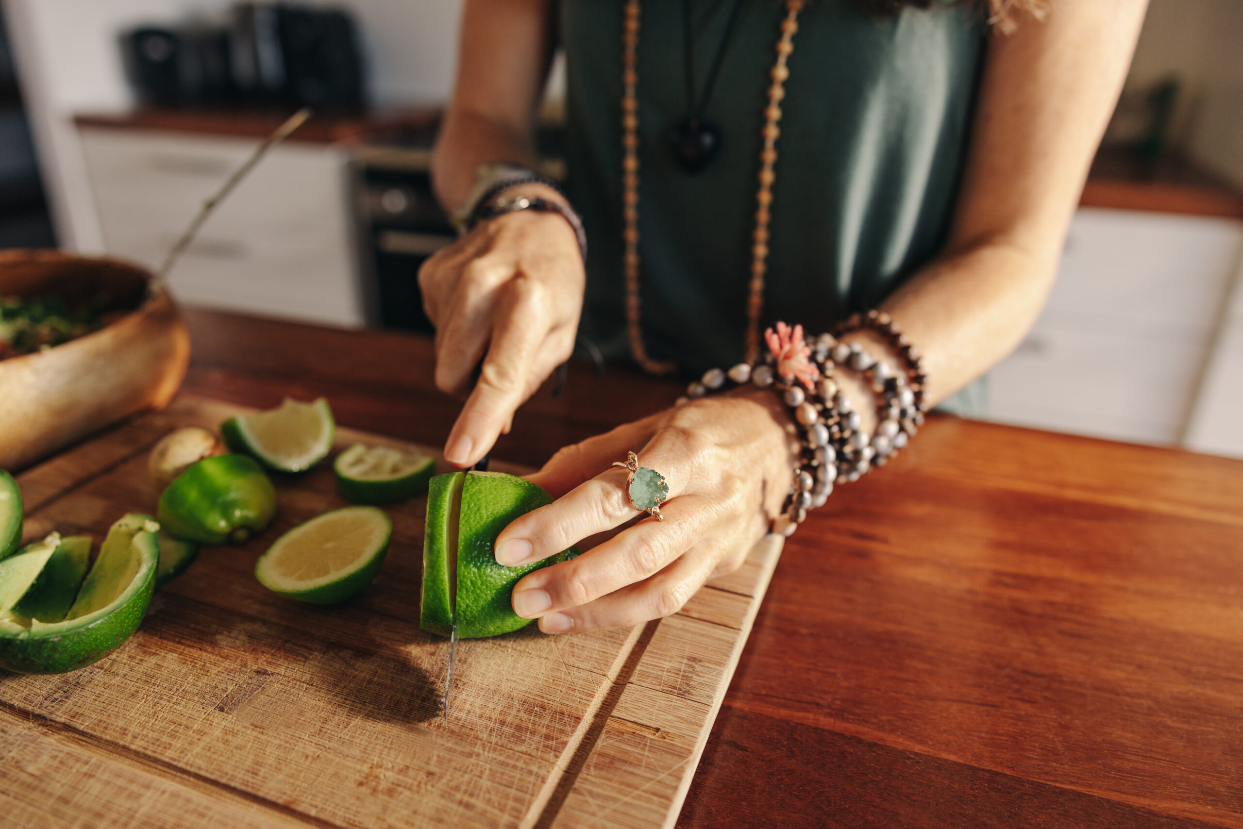 Vegetarian senior woman cutting some limes for green juice in her kitchen. Mature woman preparing a healthy plant-based meal at home. Woman taking care of her aging body with an organic diet.